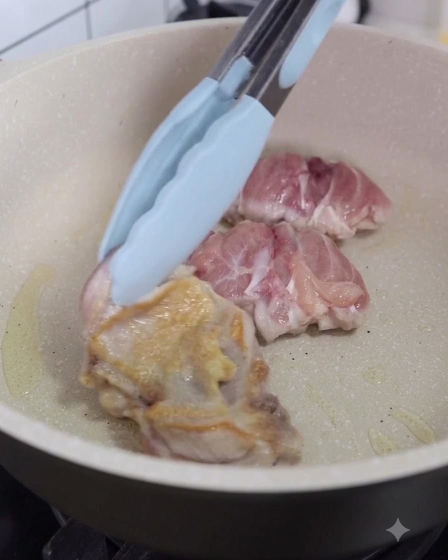 フライパンの中の鶏肉をキッチントングで裏返している様子。
