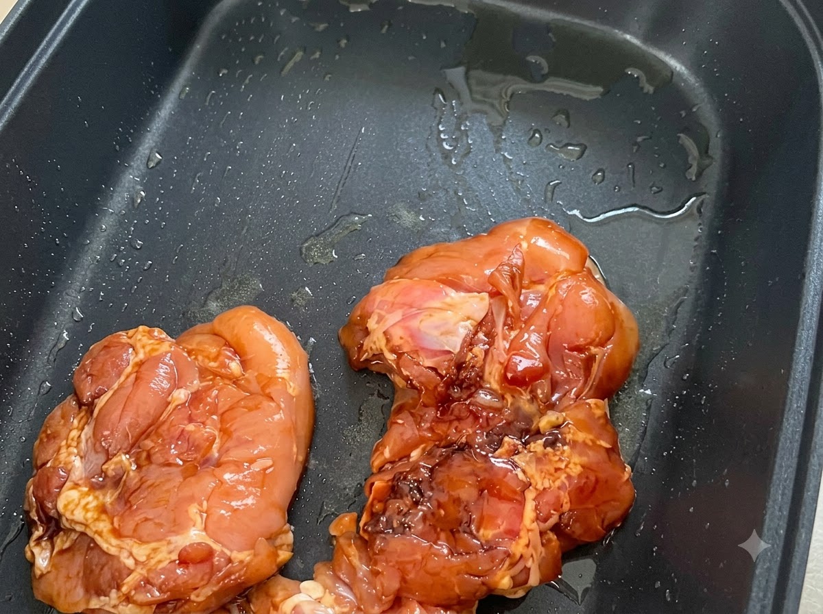 油を引いた黒いノンスティック加工のフライパンに、皮を下にして並べられた味付け済みの鶏肉。