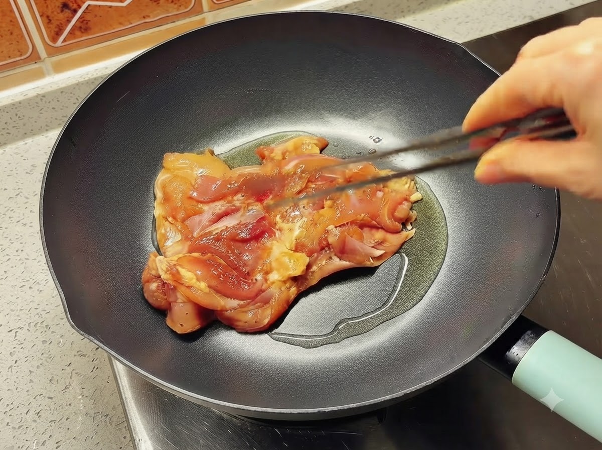 トングを使って、油をひいた熱々のフライパンに下味をつけた鶏もも肉を1枚入れる様子。