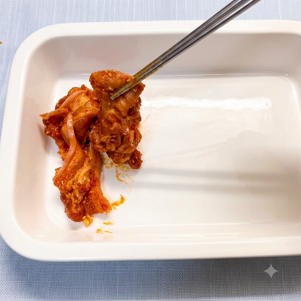 箸を使って、下味をつけた豚バラ肉のスライスを白いセラミック製の耐熱皿に1枚ずつ並べている様子。
