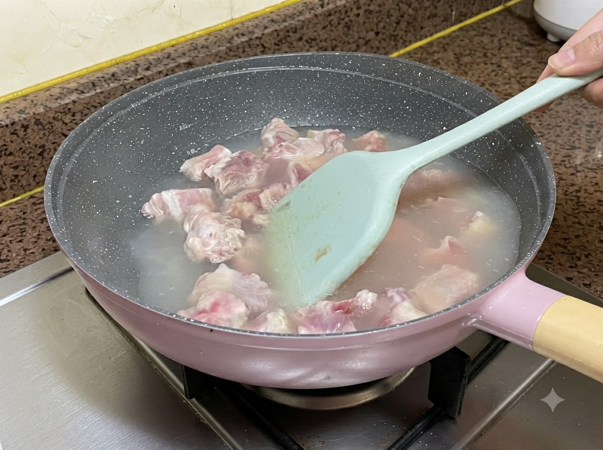 ライトブルーのシリコンスパチュラでかき混ぜながら、鍋の中の湯で茹でられている豚スペアリブ。
