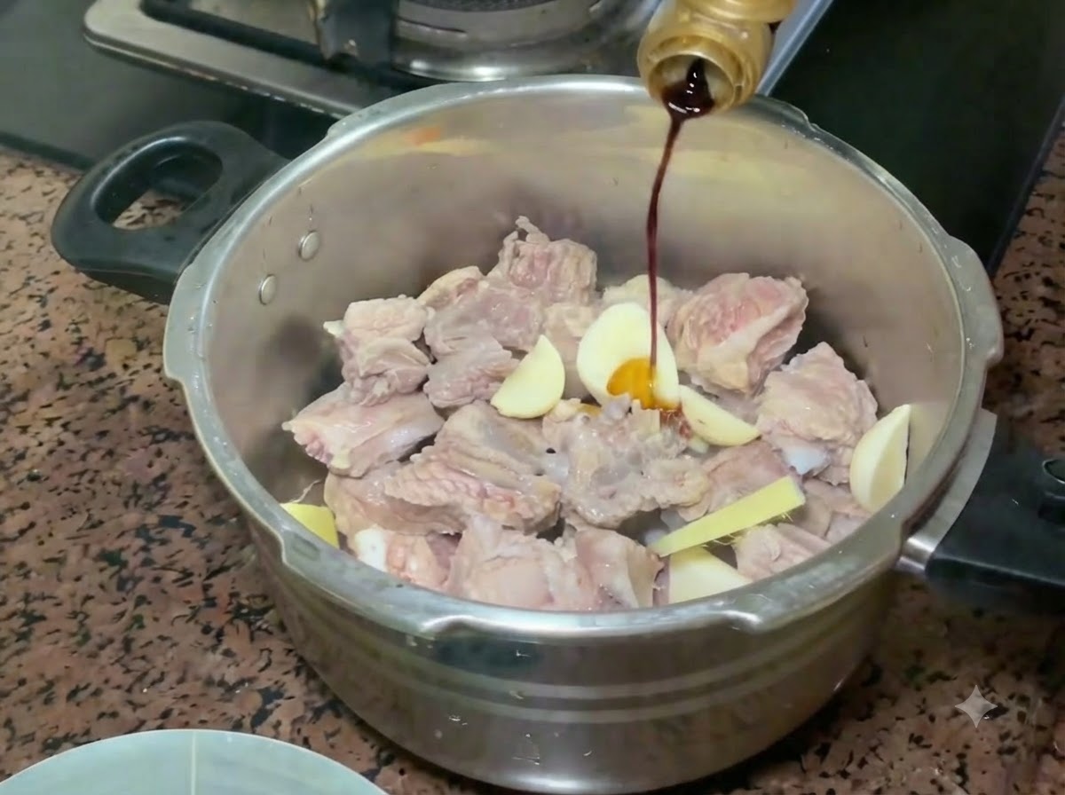 圧力鍋の中の豚スペアリブと香味野菜の上へ、ボトルから薄口醤油が注がれている様子。