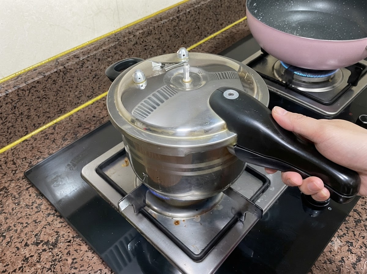 コンロのバーナー上でハンドルを握りながら、蓋がしっかりと閉じられた圧力鍋。