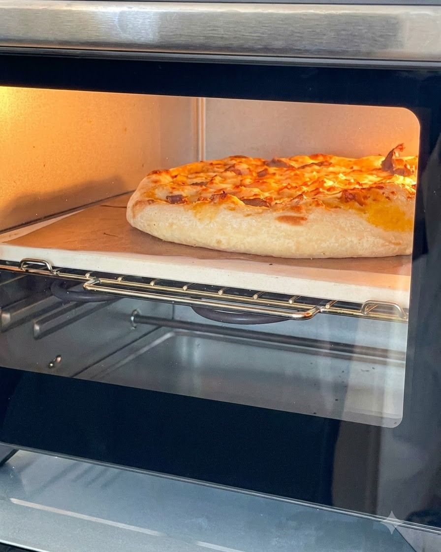 小型卓上オーブンのピザストーン上で、チーズがとろけた黄金色の焼き上がりピザ。