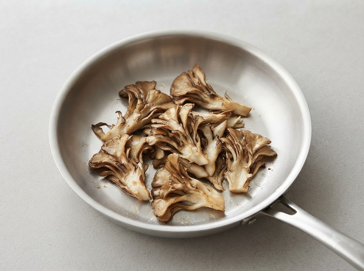 清潔なフライパンの中で、手でほぐしたマイタケを香ばしく焼き上げている様子。