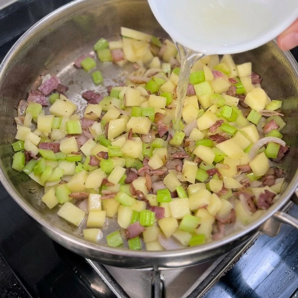白いボウルから、ソテーした野菜とベーコンの入ったフライパンに透明なアサリの出汁が注がれている様子。