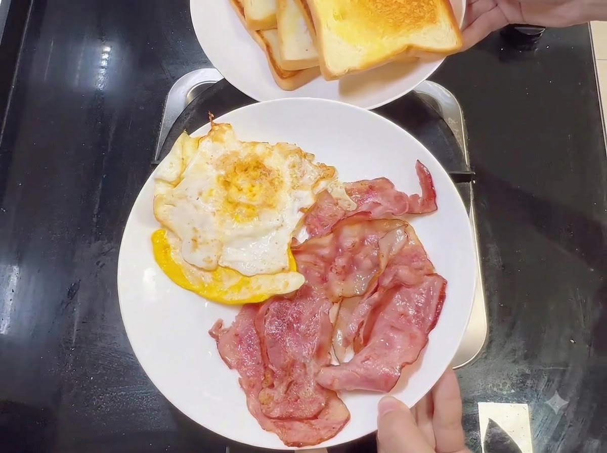 調理済みのベーコンと目玉焼きが乗った白いお皿と、その上に掲げられたトーストの皿。