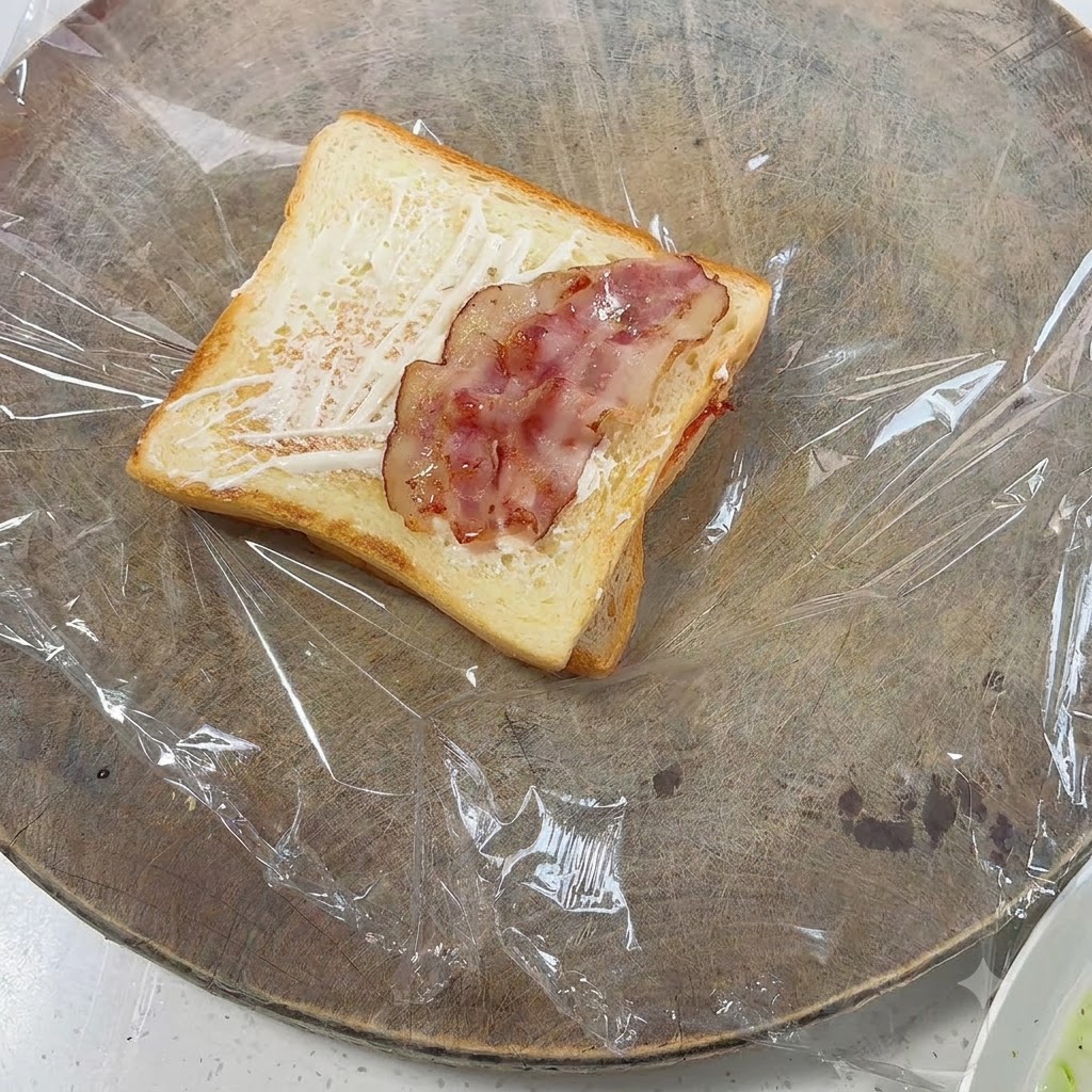 マヨネーズを塗ったトーストの上にきれいに並べられた調理済みベーコンのピース。