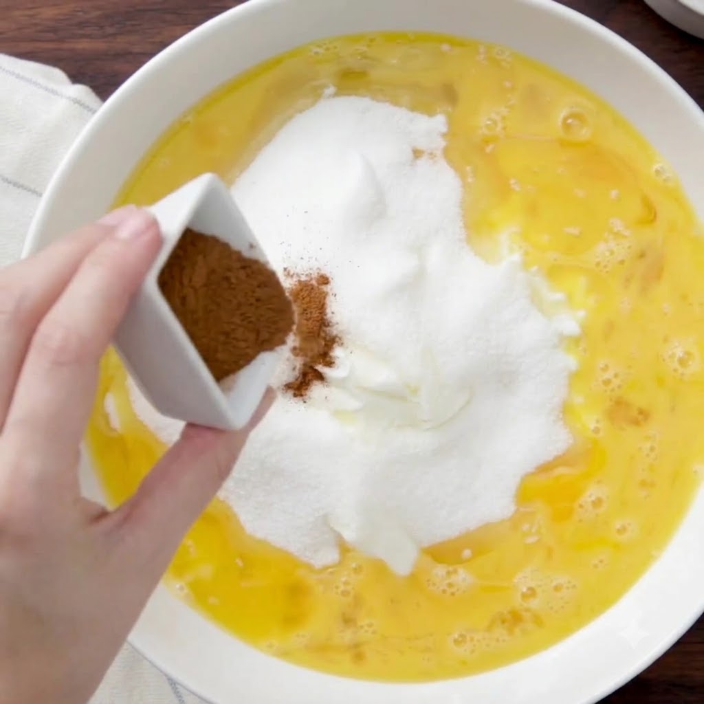 四角い小さな器から、シナモンパウダーが材料の混ぜ合わせに振りかけられている様子。