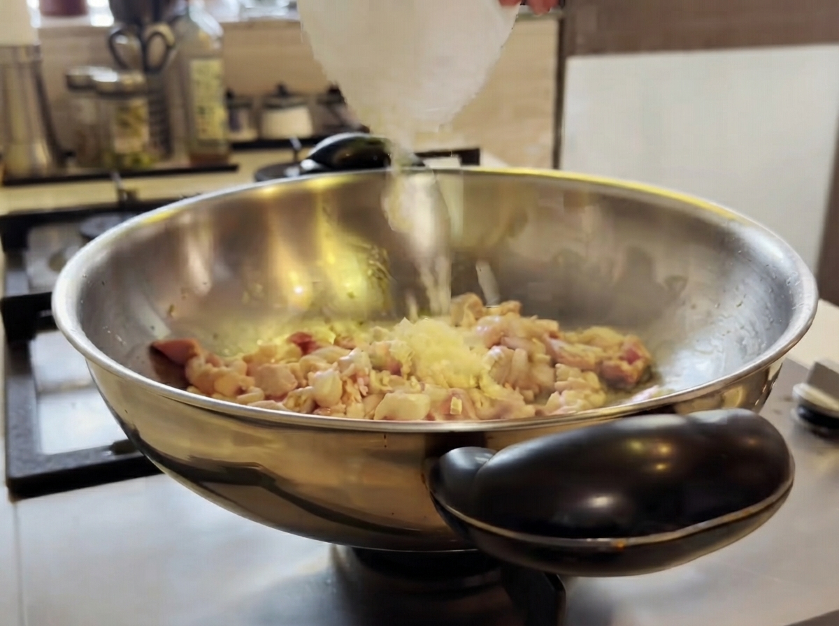 調理中の鶏肉が入った中華鍋に刻みニンニクが加えられ、ヘラで混ぜ合わせられている様子。