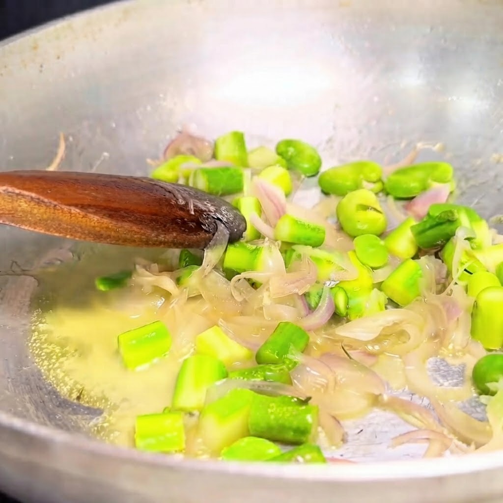 金属製のフライパンから、木べらを使って炒めた玉ねぎと緑黄色野菜をすくい出している様子。