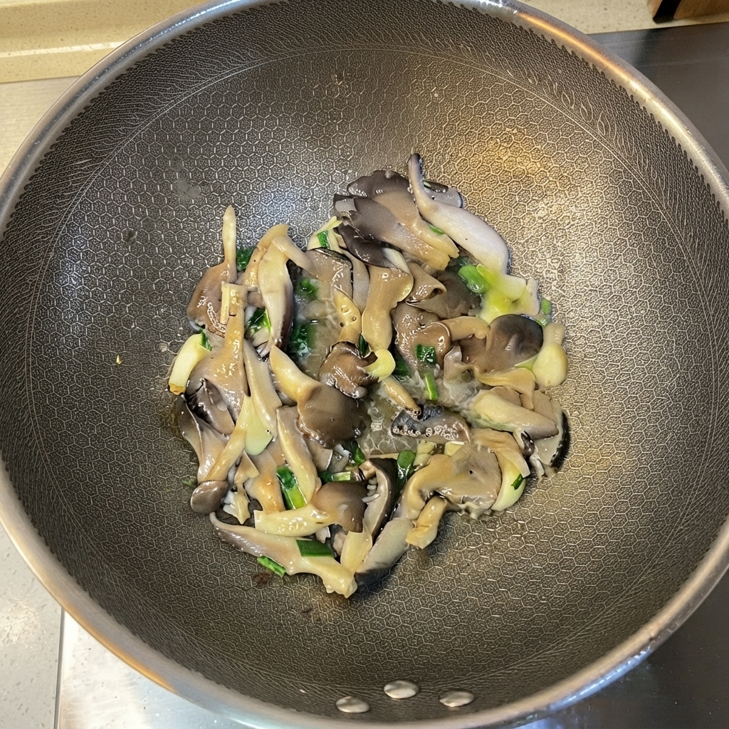 炒めたエリンギと香味野菜を中華鍋の中で混ぜ合わせている様子。