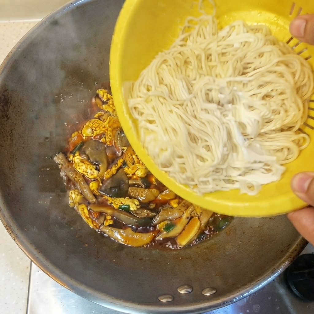 黄色いザルから茹でた細麺を、タレや具材の入った中華鍋に移している様子。