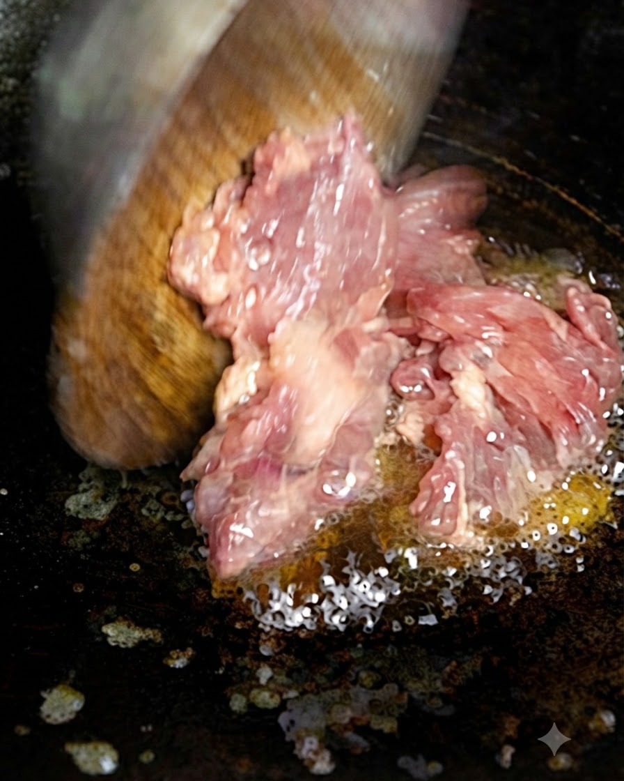 木製スパチュラを使い、熱したフライパンの油に刻み肉を入れている様子。
