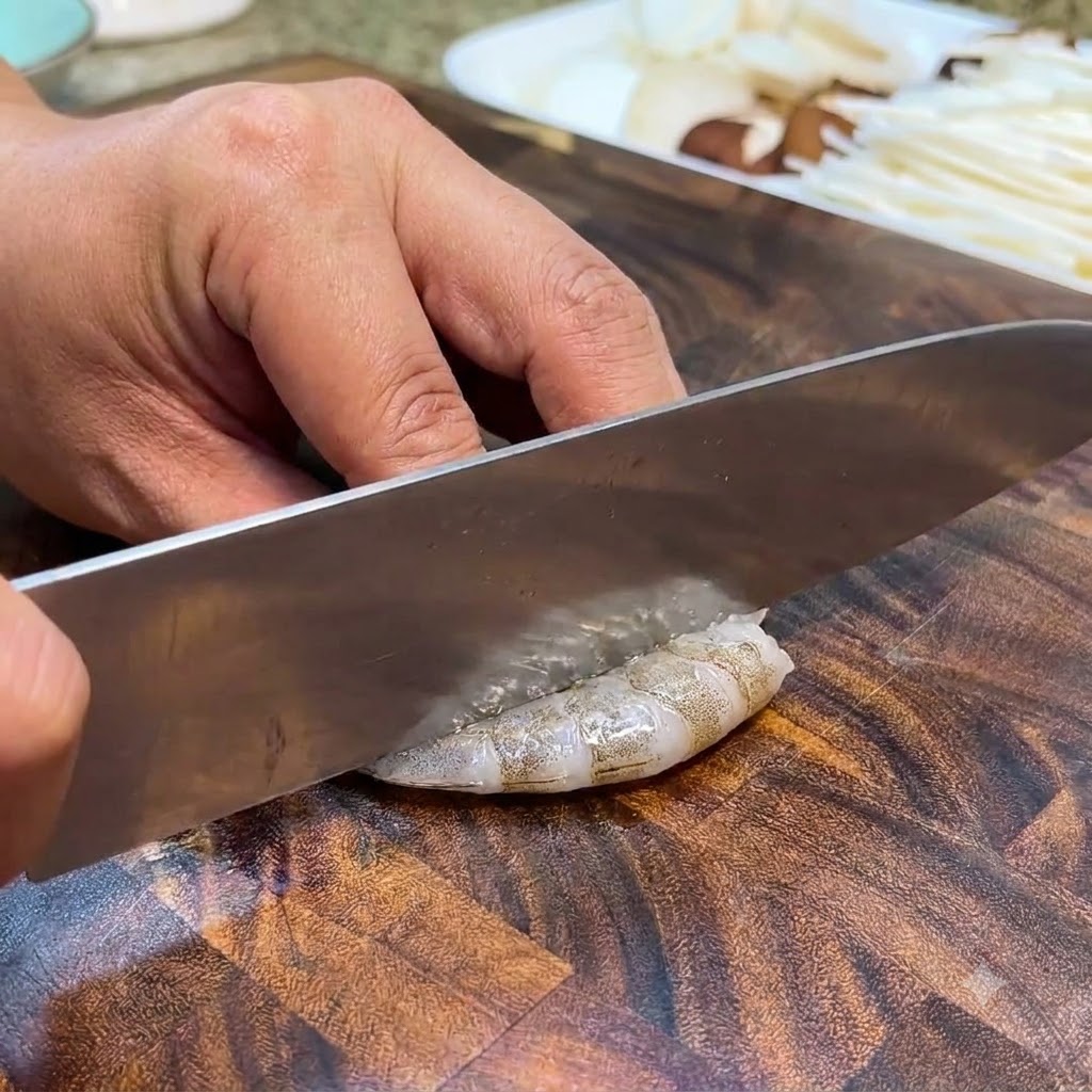 木製のまな板の上で、ナイフを使ってエビの背わたを取り除いている様子