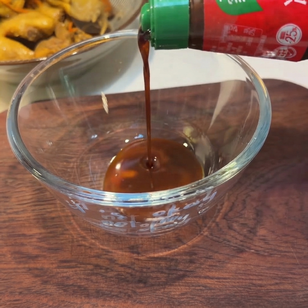 木製の台の上で、緑色のキャップのボトルから透明なガラスの丼に注がれる黒いタレ。