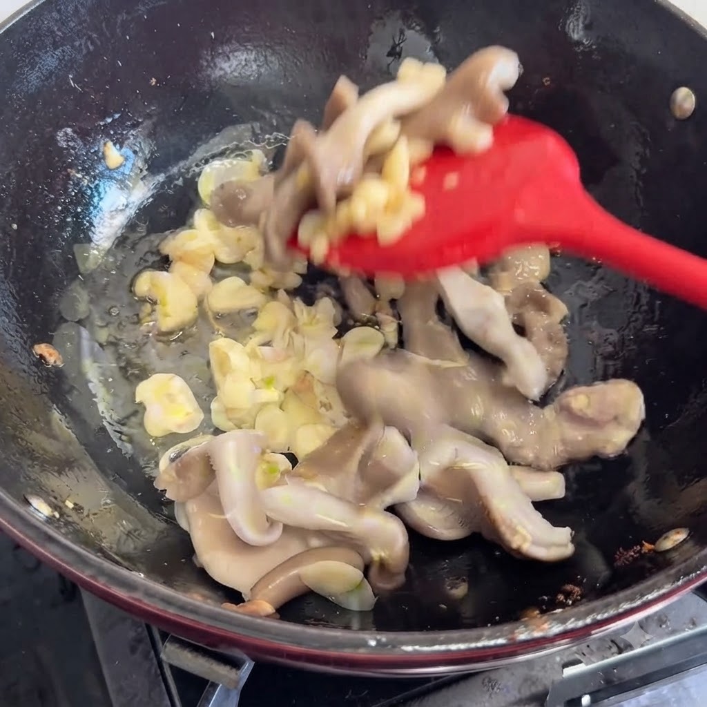 赤いスパチュラを使い、香味野菜と一緒に生キノコをフライパンに加えて炒めている様子