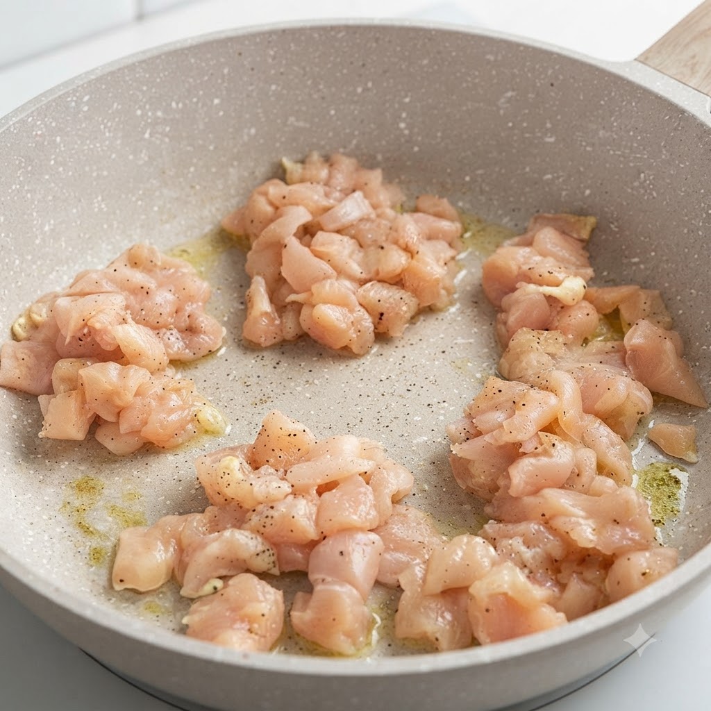 弱火にかけた丸いフライパンの中で、下味をつけた鶏むね肉のピースがジューシーに焼けている様子。