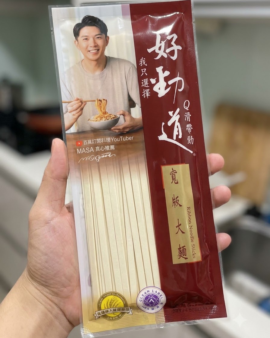キッチンの背景を前に、麺のパッケージが持たれている様子。