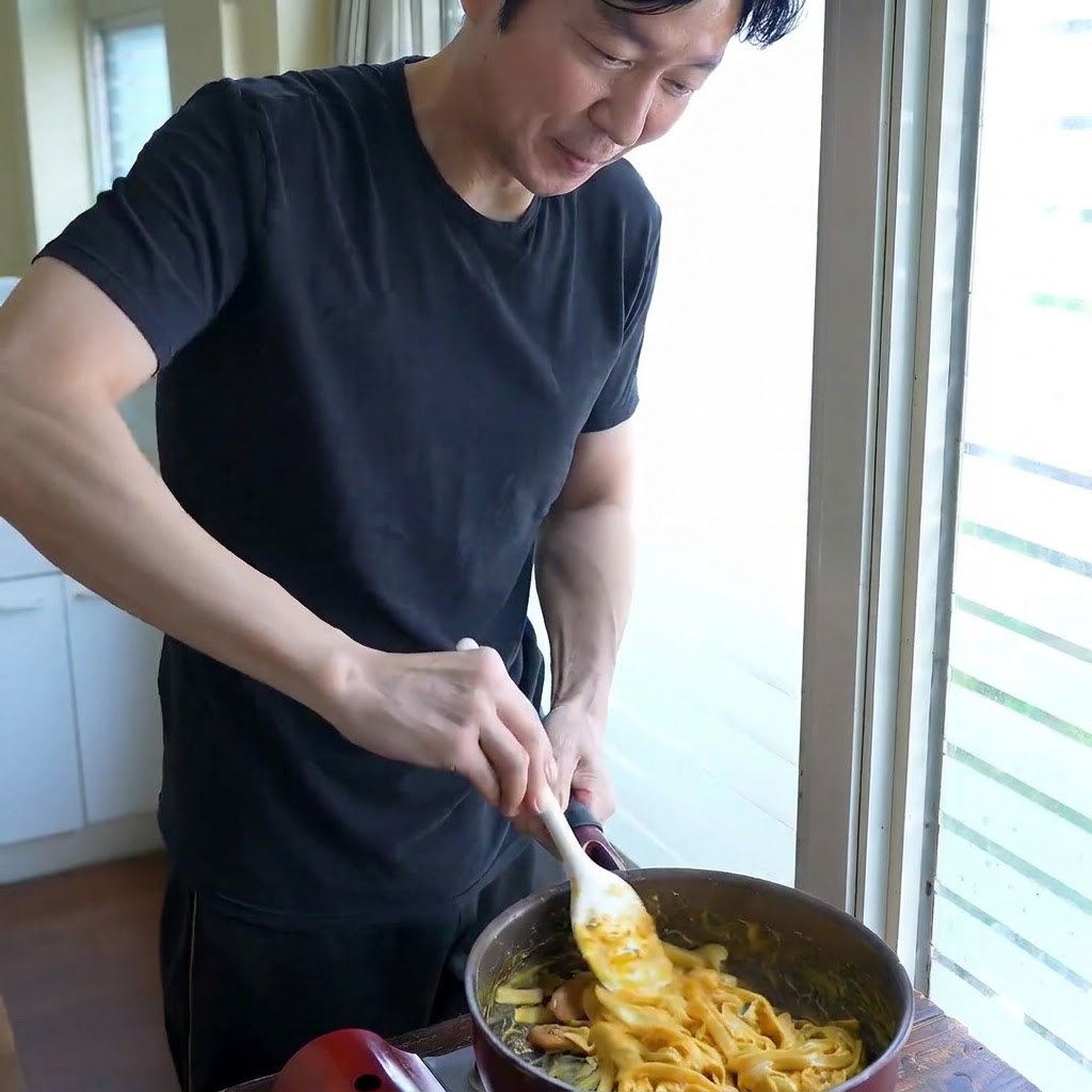 白いスパチュラを使い、フライパンの中でソースと幅広麺を混ぜ合わせながらとろみを調整している様子。