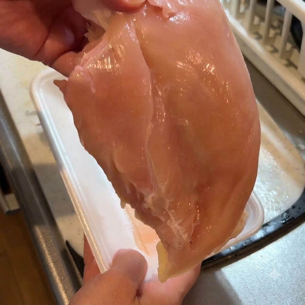 包丁を使って鶏胸肉の皮を剥ぎ取っている手元の様子