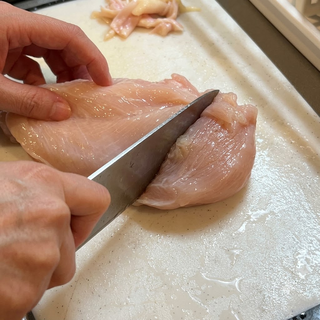 まな板の上に置かれた鶏胸肉に包丁で細かく穴を開けている様子