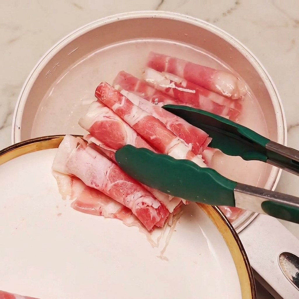 トングを使い、ネギの切り身を入れた沸騰したお湯の鍋に冷凍の薄切り牛肉を入れている様子。