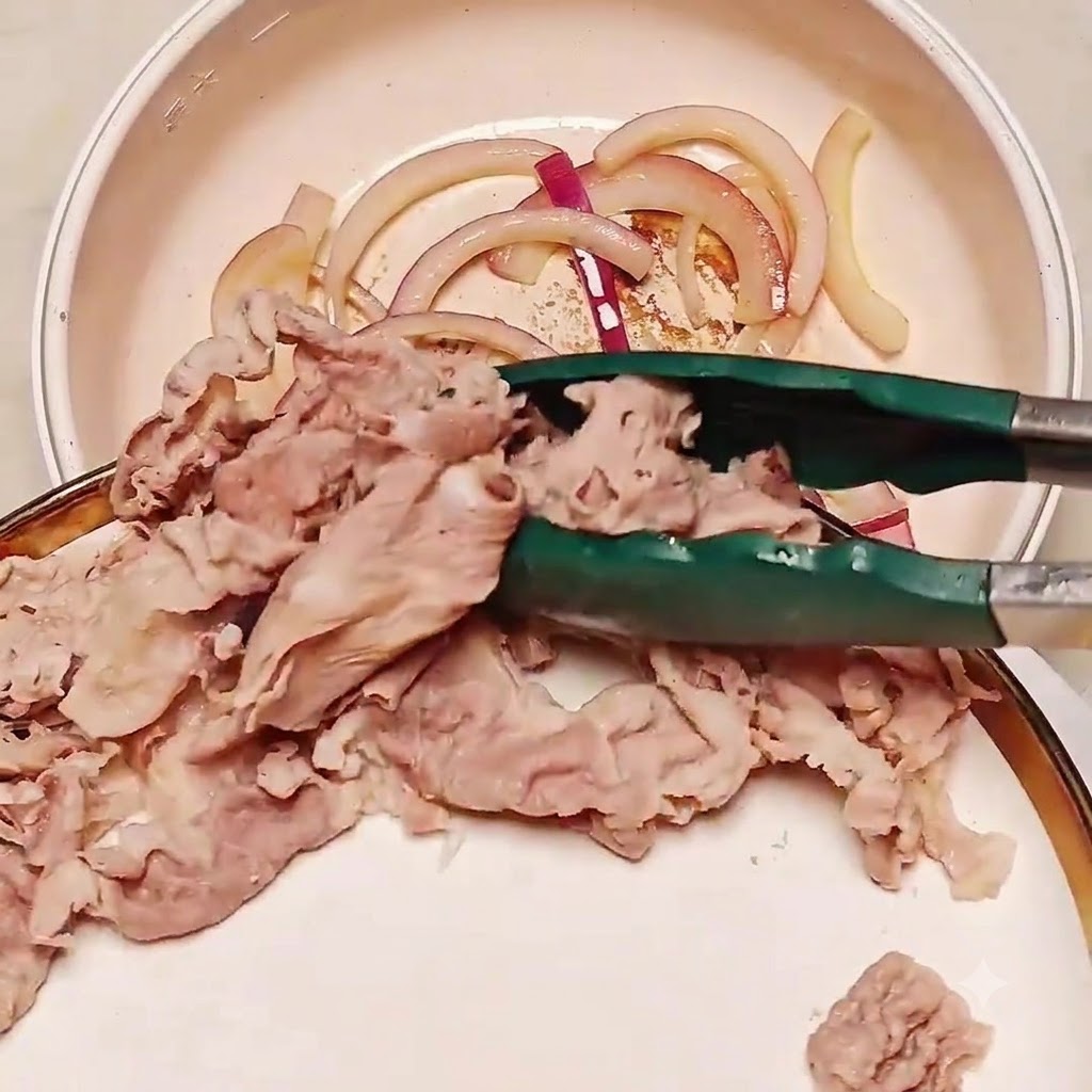 トングを使って、下茹で済みの牛肉のスライスを炒めた玉ねぎの入ったフライパンに移している様子。