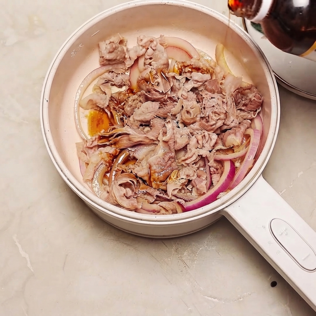 牛肉と赤玉ねぎが入ったフライパンに、ボトルからすき焼きのタレが注がれている様子。