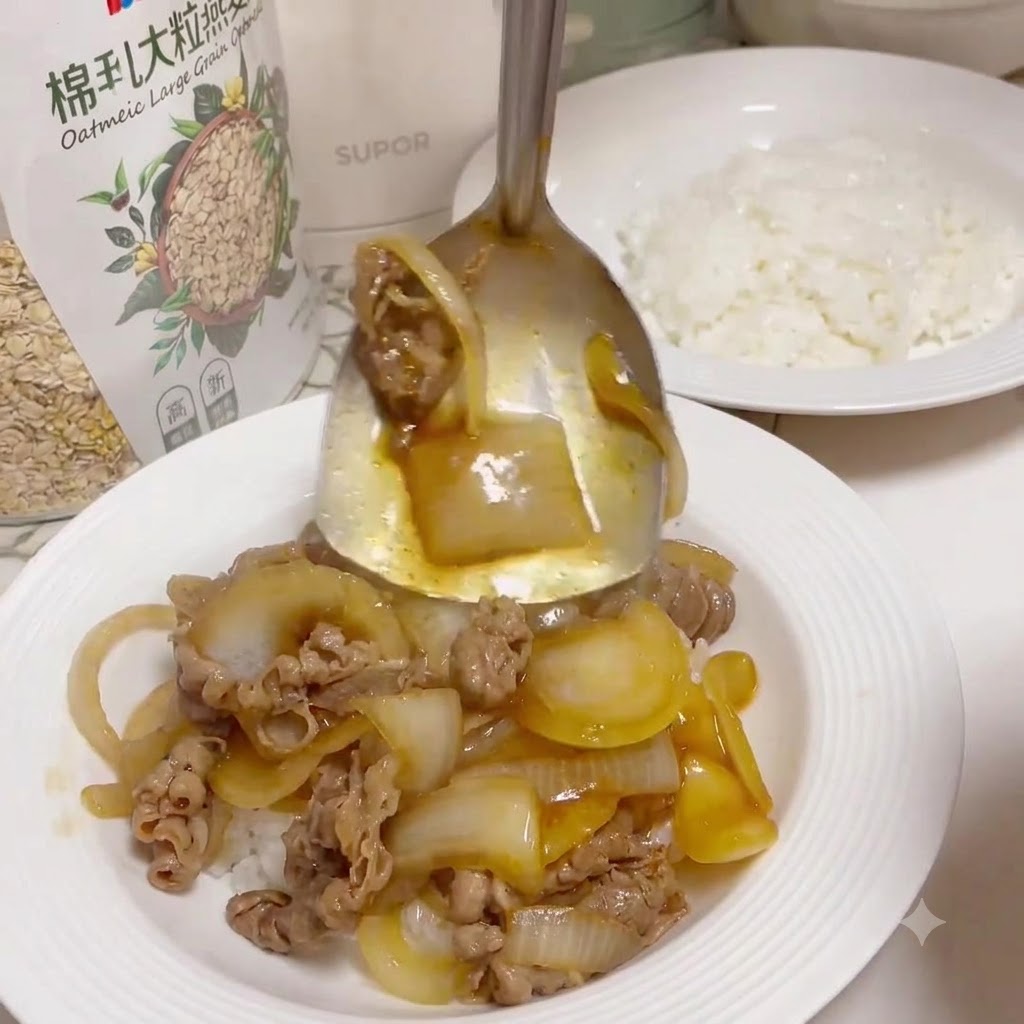 調理された白いご飯が入った皿の上に盛り付けるために、フライパンから火を通した牛肉とツヤのあるタマネギをすくう金属製のサービングスプーン。