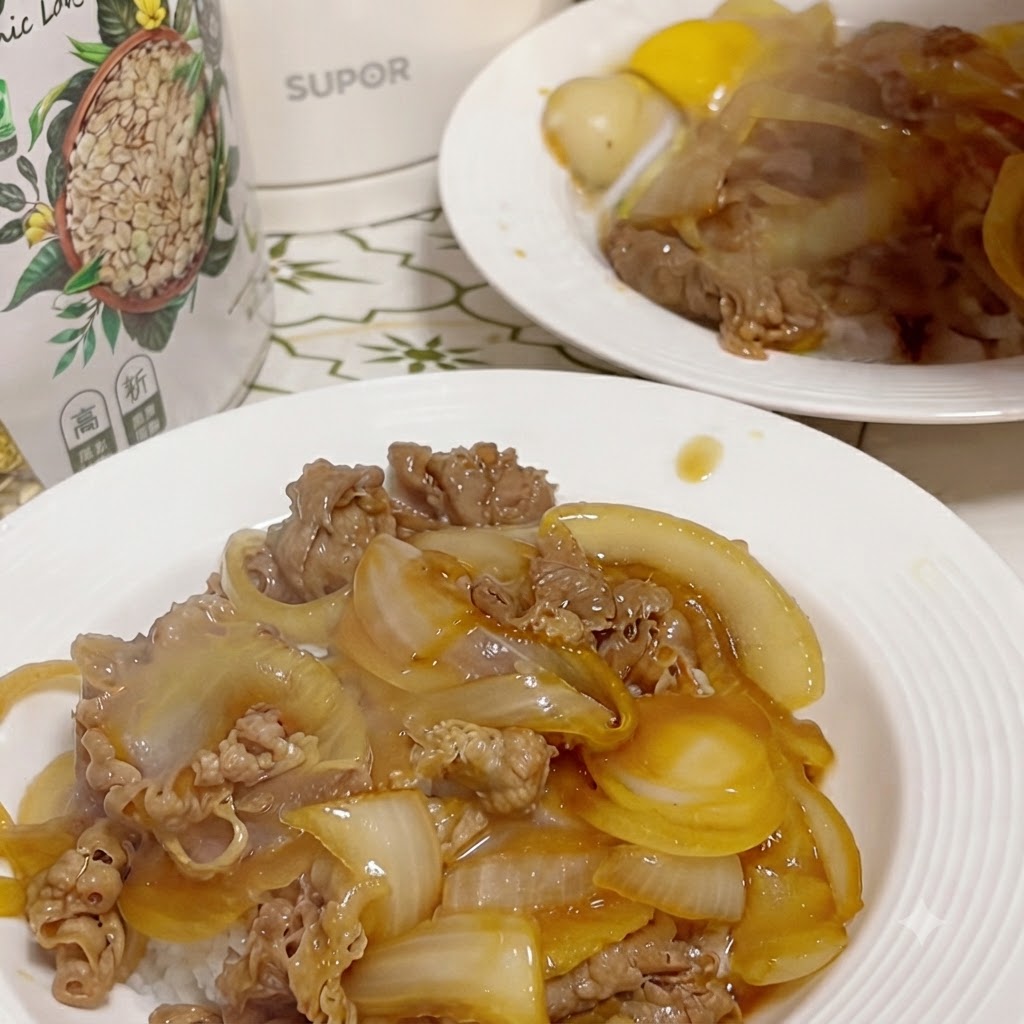 中央に作られた小さな窪みに割られた生卵の黄身がのせられた、牛肉とタマネギのご飯の完成した一皿(背景には2皿目もうっすら見える)。