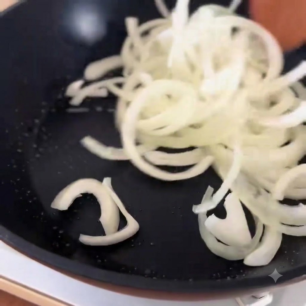 フライパンで炒めた玉ねぎの上に、先ほど下茹でした牛肉を広げている様子。