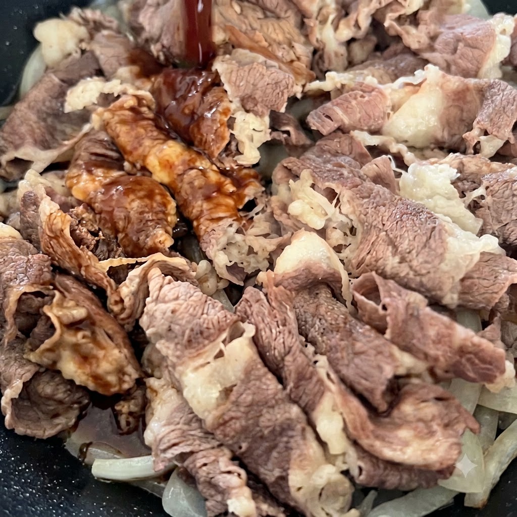 フライパンの牛肉と玉ねぎめがけて、上から濃い色のタレを注ぎ入れている様子。