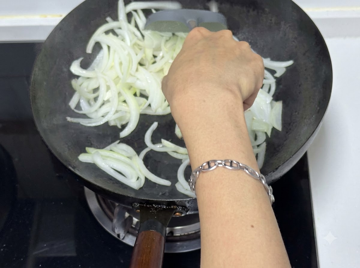 スパチュラを使って中華鍋で玉ねぎを炒め、半透明で少しきつね色になった状態。