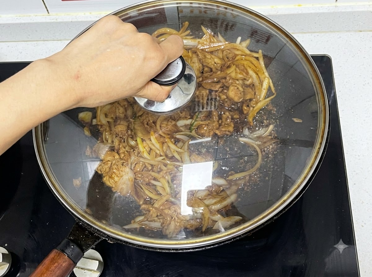 牛肉と玉ねぎを煮込んでいる中華鍋にガラスの蓋を置く様子。