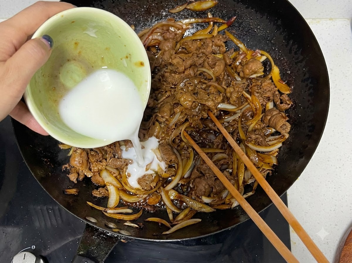 小さなボウルから水溶き片栗粉を中華鍋に注ぎ入れる様子と木の菜箸。