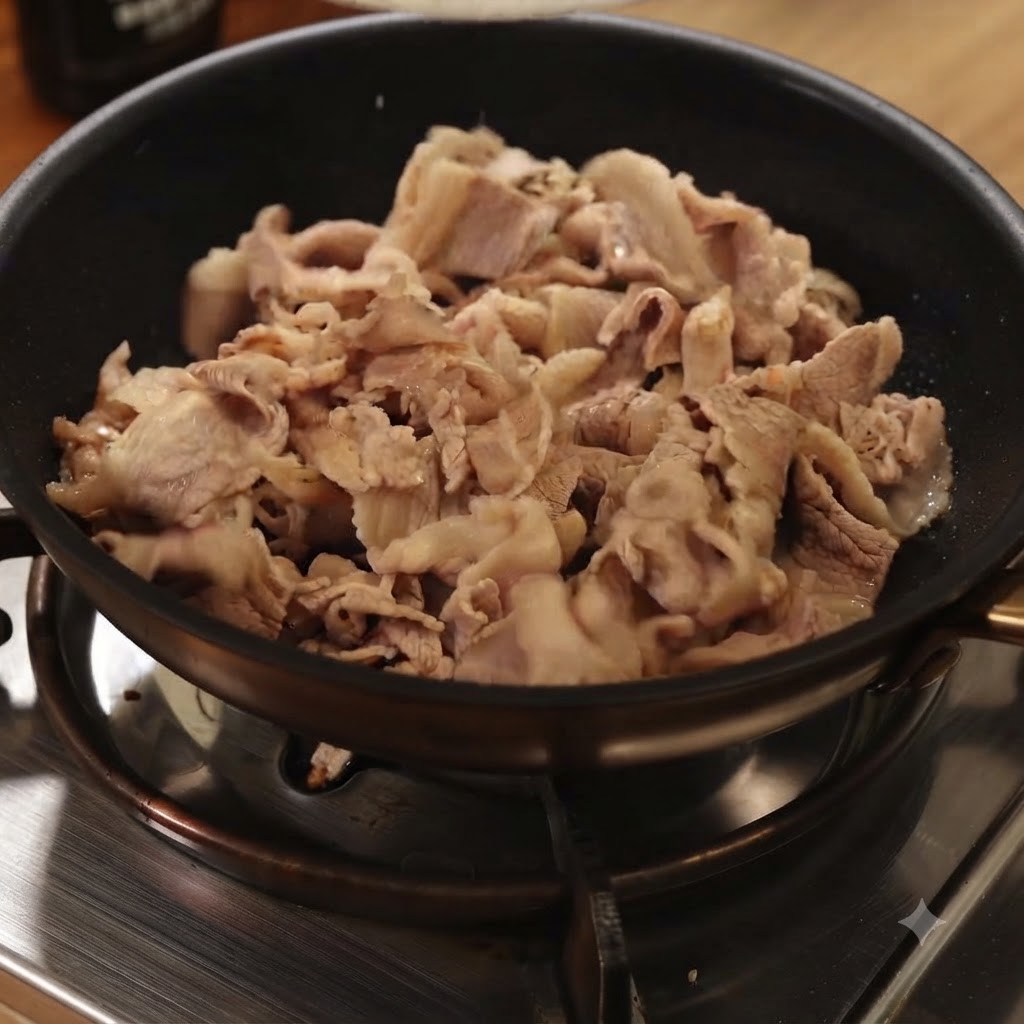 ガスコンロの上の黒いフライパンで、湯通しした牛肉を炒めているところ