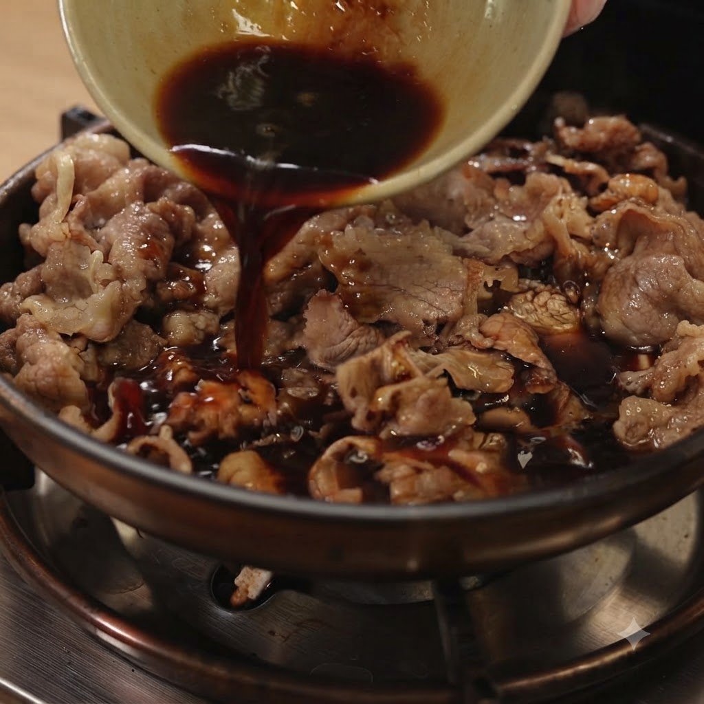 スライスした牛肉と赤玉ねぎが入ったフライパンに、小さな器から黒い照り焼きダレを注いでいるところ