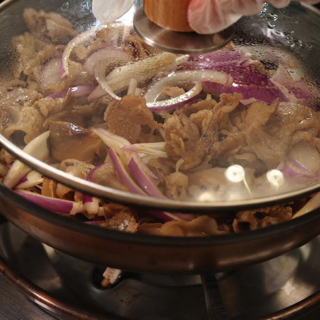透明なガラス蓋が閉められ、牛肉と赤玉ねぎが中で煮込まれているフライパン