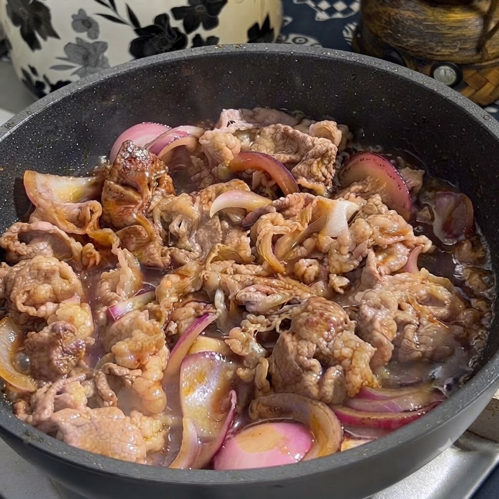 容器からテリヤキソースを、炒めた牛肉と赤玉ねぎの入ったフライパンに注いでいる様子
