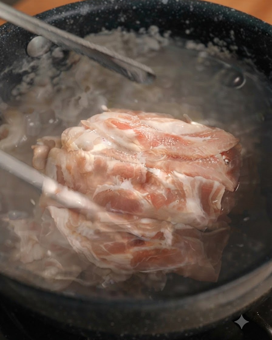 トングで沸騰した鍋から下茹でされた牛肉の薄切りを持ち上げている様子。