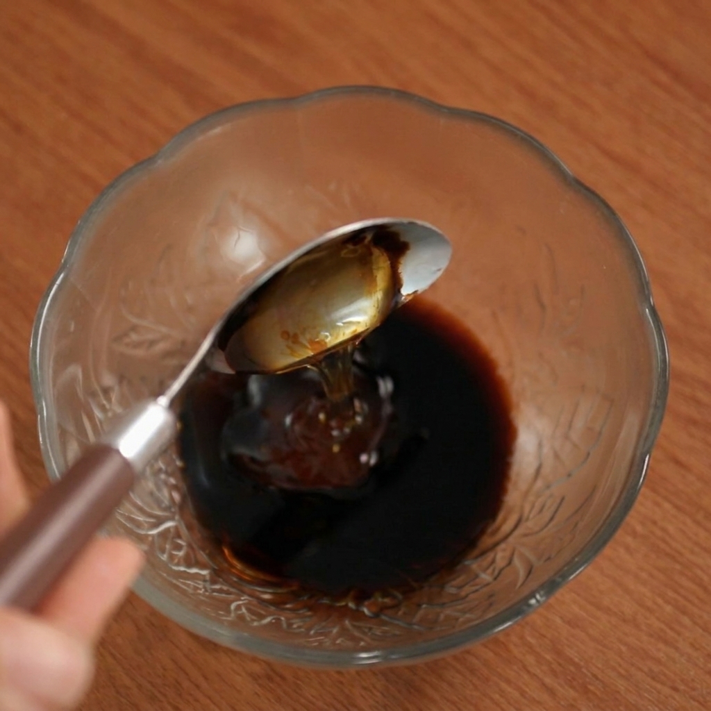 ガラスボウルの中の濃い色のソースに、スプーンからハチミツを垂らしている様子。