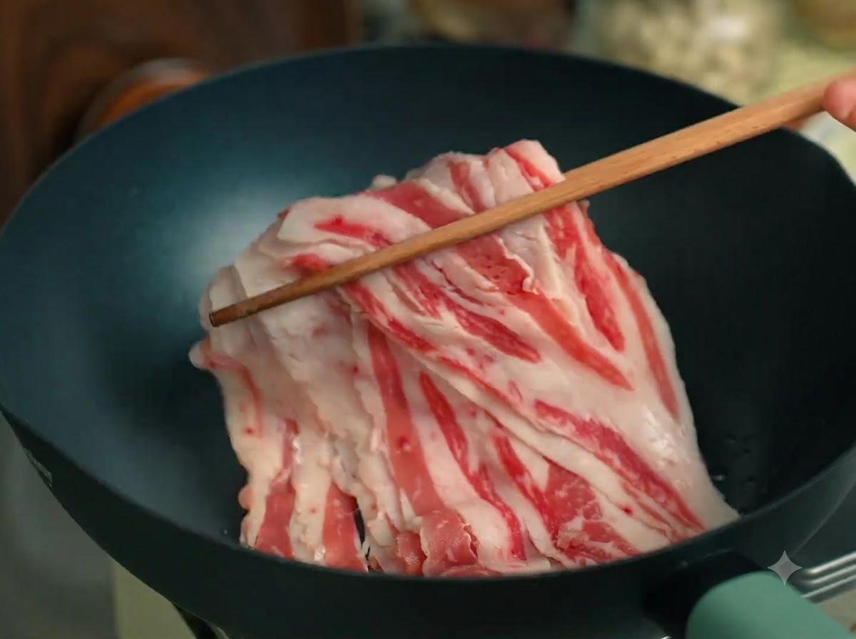 黒いフライパンの中で、牛脂が木製の箸で炒められている様子。