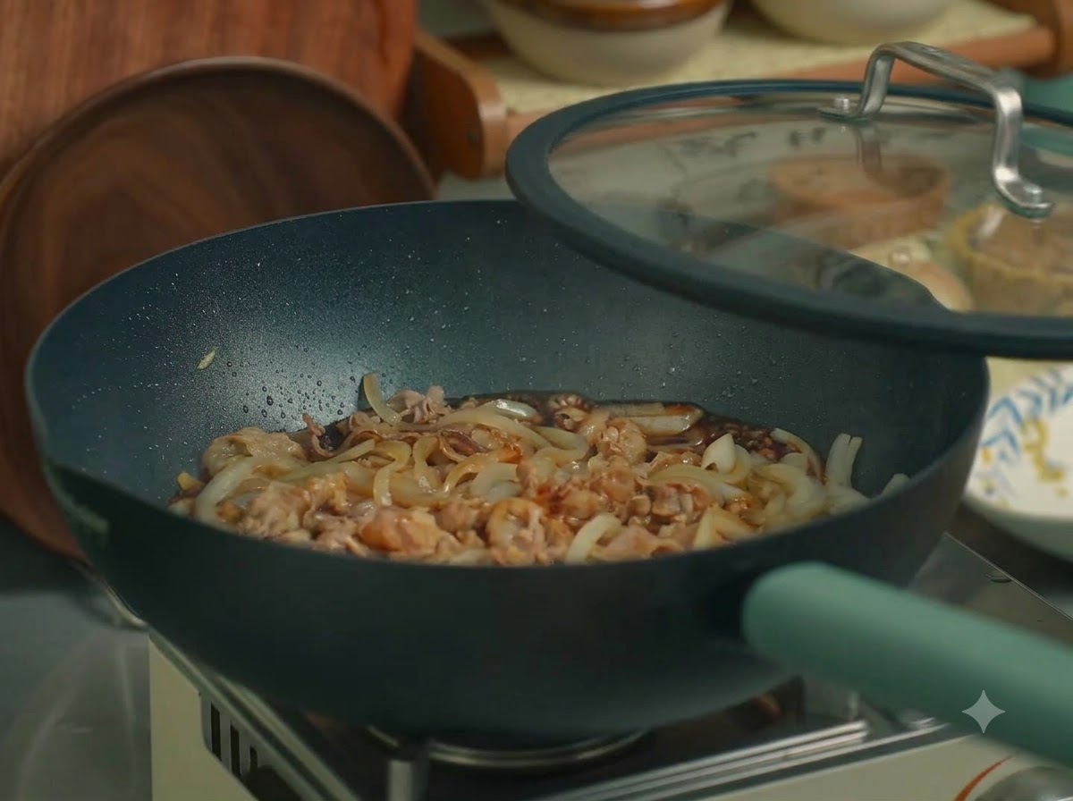 牛肉と玉ねぎが入ったフライパンにガラスの蓋がされ、コンロの上に乗っている様子。