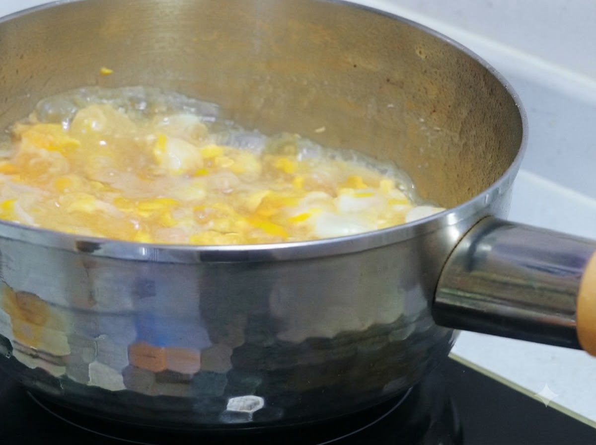 鶏肉と玉ねぎが入った鍋に、軽く溶いた卵液を流し入れる様子