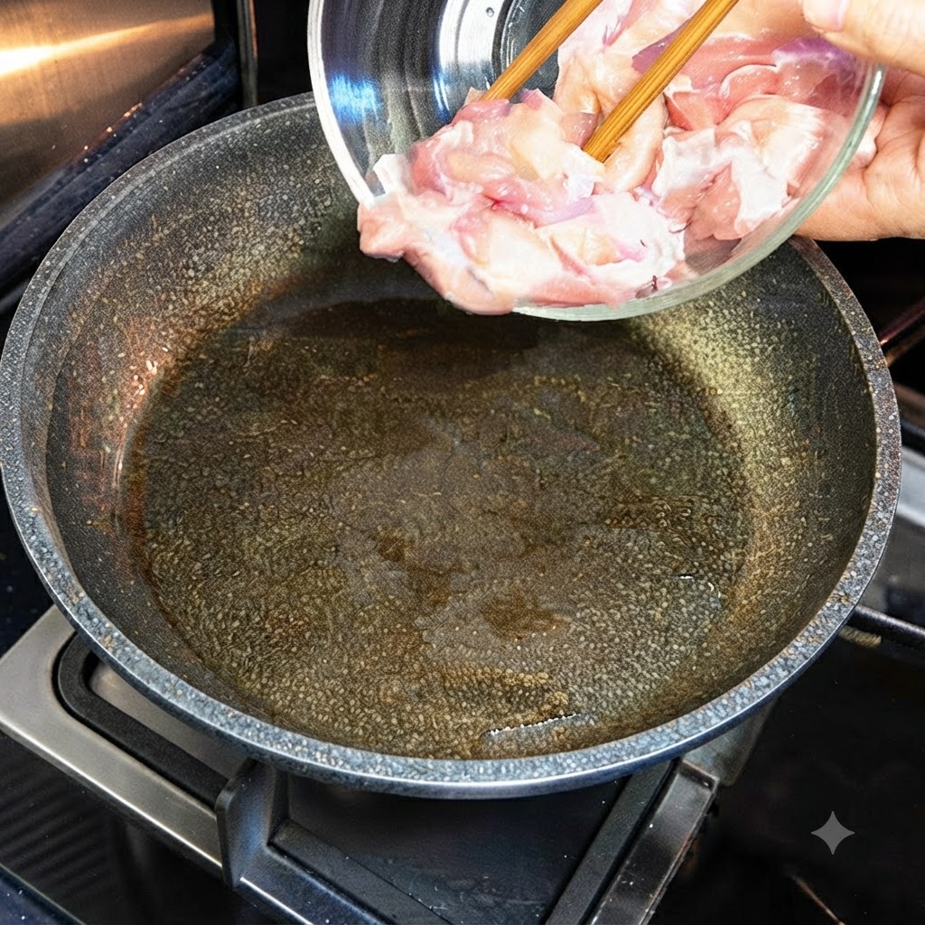 ガラスボウルから、油を引いて熱したフライパンに生の鶏肉を移しているところ。