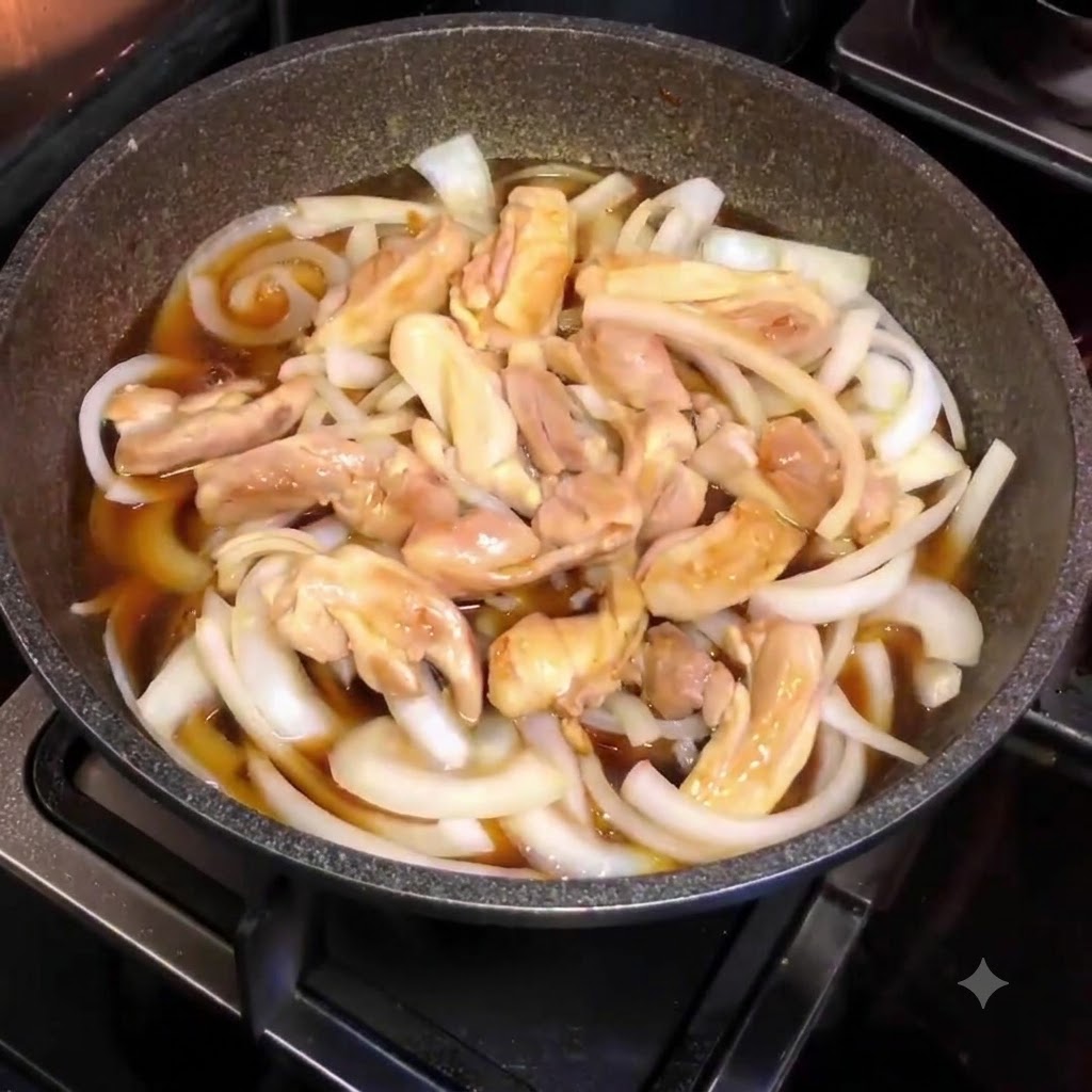 上から撮影した、スライスした玉ねぎ、鶏肉、茶色のタレが入った煮込み中のフライパン。