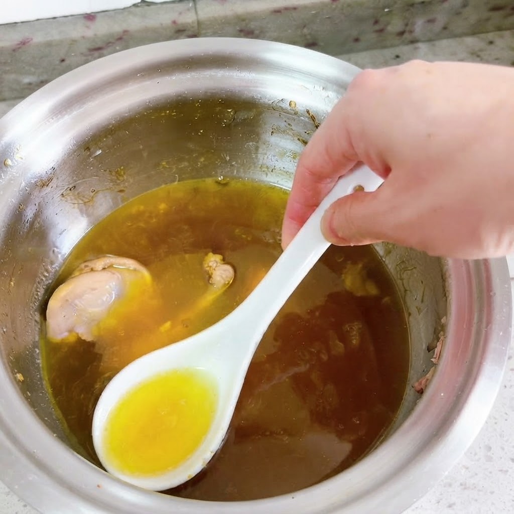 白いスプーンを使って、煮込んでいるアヒルのスープの表面から鮮やかな黄色の油をすくい取っているところ。