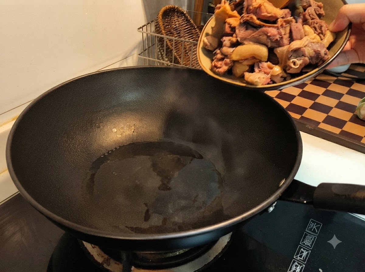 油を引いた熱した黒い中華鍋に、皿から湯通しした鴨肉を投入している手。
