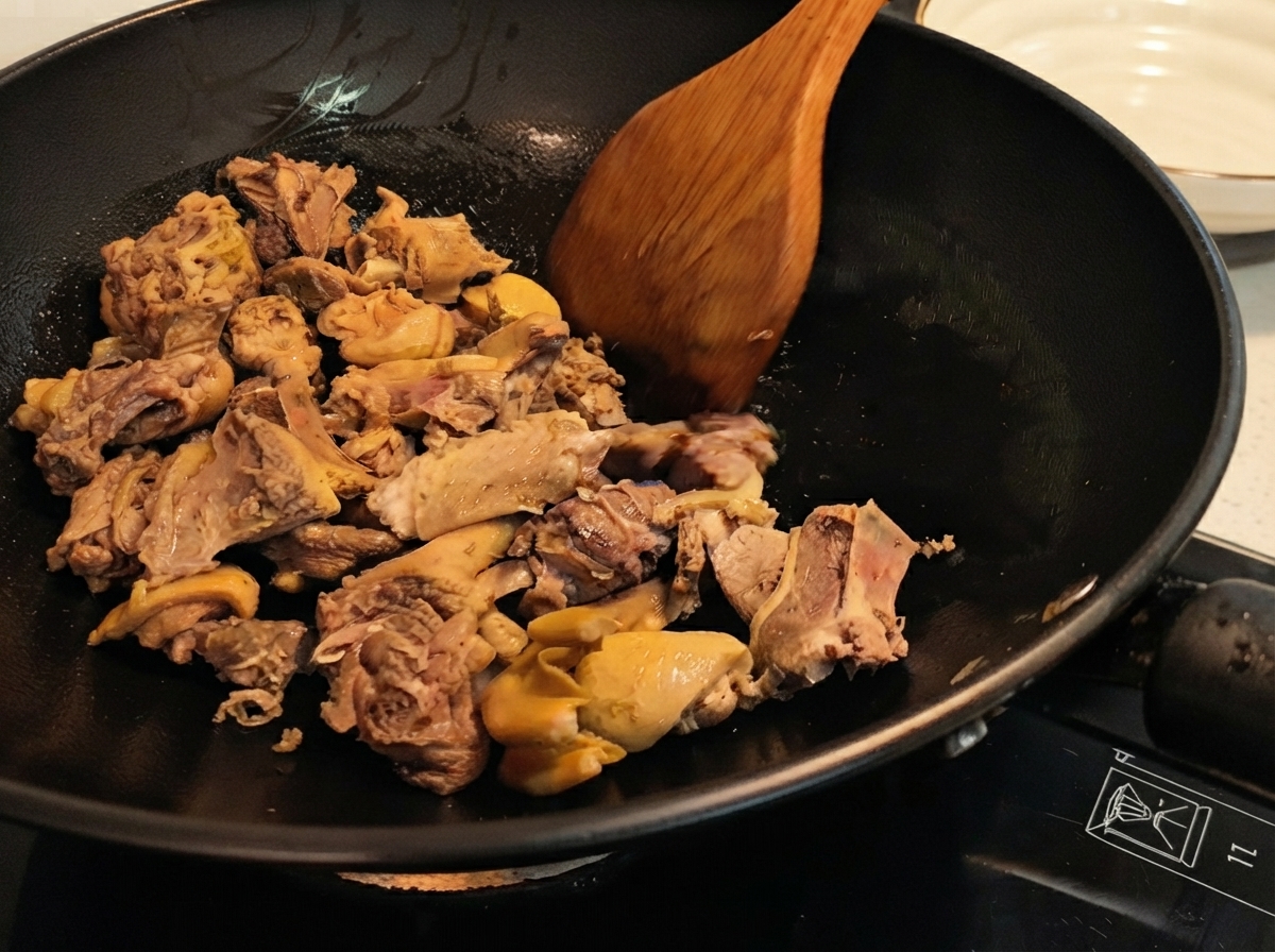 木べらを使って中華鍋の中で鴨肉を炒め合わせており、皮がこんがりと焼け始めている様子。